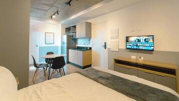 Una habitación de hotel moderna con cama, televisión, escritorio y kitchenette.