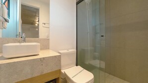 Casa de banho moderna com lavatório branco, sanita e cabine de duche em vidro.