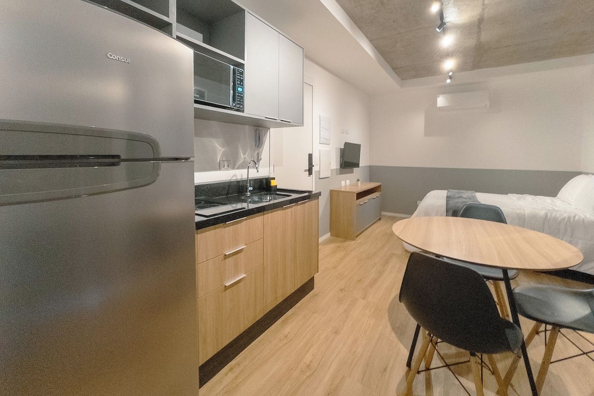 A compact kitchen with a refrigerator, microwave, and wooden cabinets. There is a small dining area with a table and chairs.