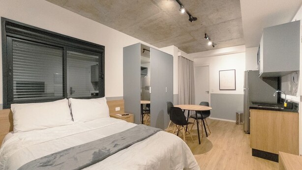 Quarto de hotel moderno com cama grande, área de refeições e cozinha compacta.