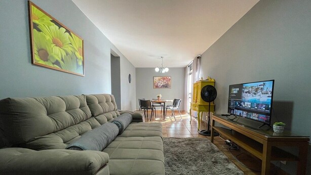 Uma sala de estar com sofá seccional, televisão de tela plana e área de jantar com cadeiras e mesa.
