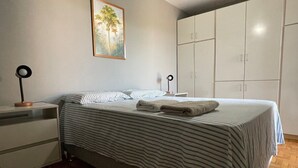 Quarto com cama, mesa de cabeceira, luminária, guarda-roupa e um quadro na parede.