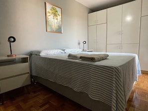 Een slaapkamer met een bed, nachtkastje, lamp, kledingkast en een schilderij aan de muur.