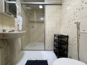 Een badkamer met een douchecabine van glas, een wastafel en een toilet.