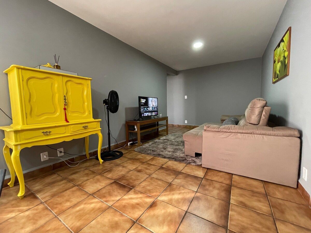 Ein Wohnzimmer mit einem gelben Schrank, einem Fernseher, einem rosa Sofa und einem Fliesenboden.
