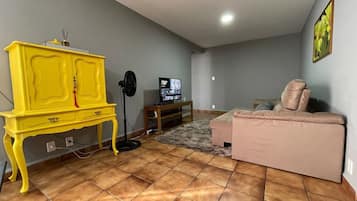 Ein Wohnzimmer mit einem gelben Schrank, einem Fernseher, einem rosa Sofa und einem Fliesenboden.