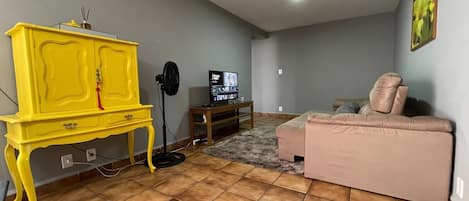 A living room with a yellow cabinet, a television, a pink sofa, and a tiled floor.