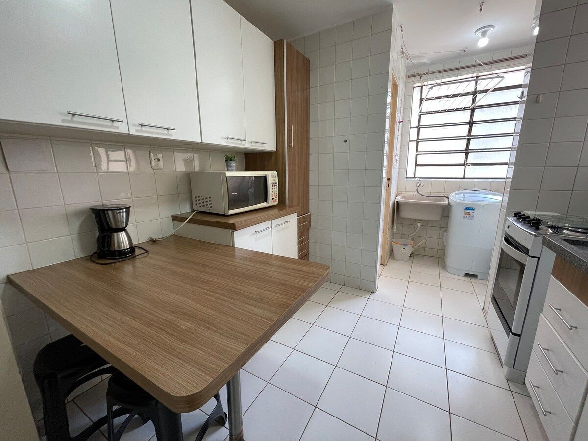 A kitchen with a wooden countertop, white cabinets, a microwave, a coffee maker, and a sink.