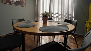 Espaço de refeições com mesa redonda, cadeiras pretas e planta em vaso.