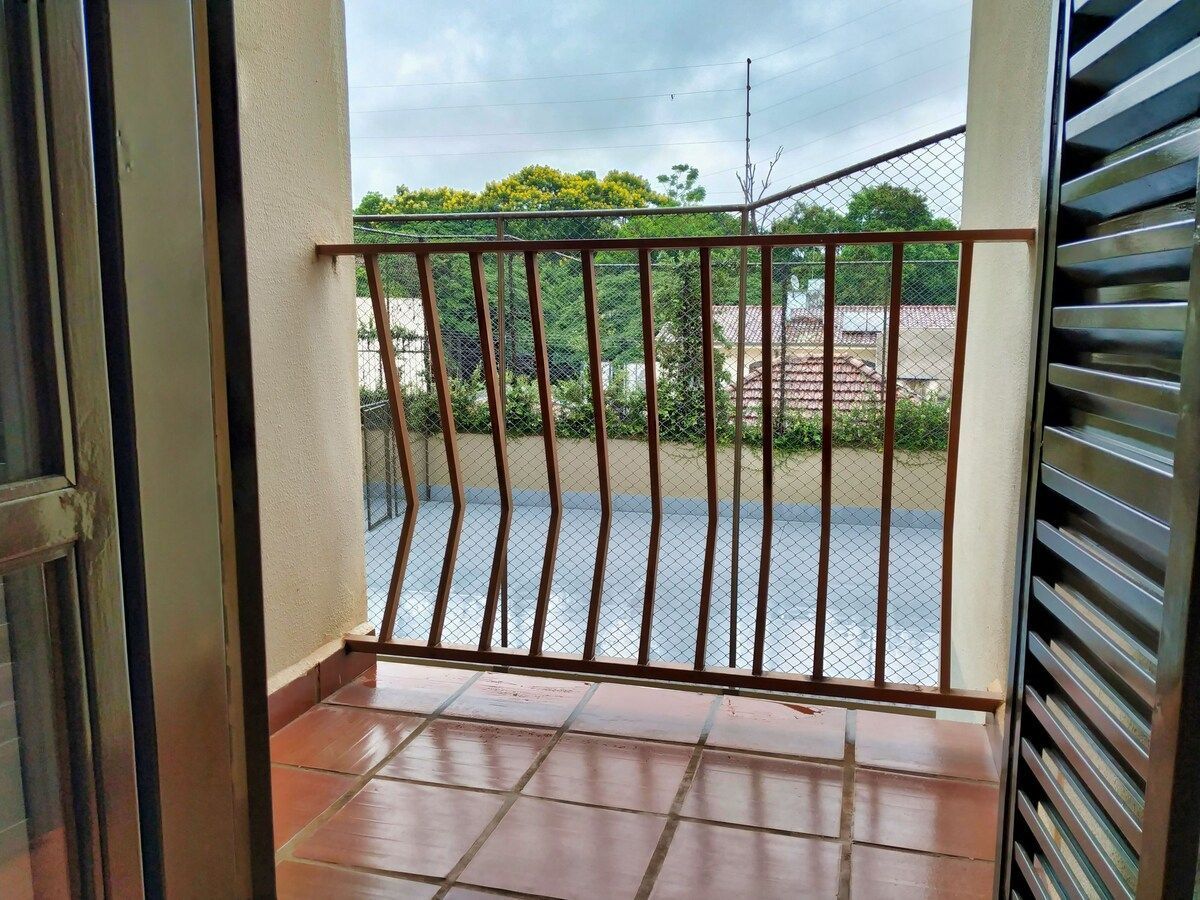 A balcony with a metal railing, a tiled floor, and a view of a fence and greenery.