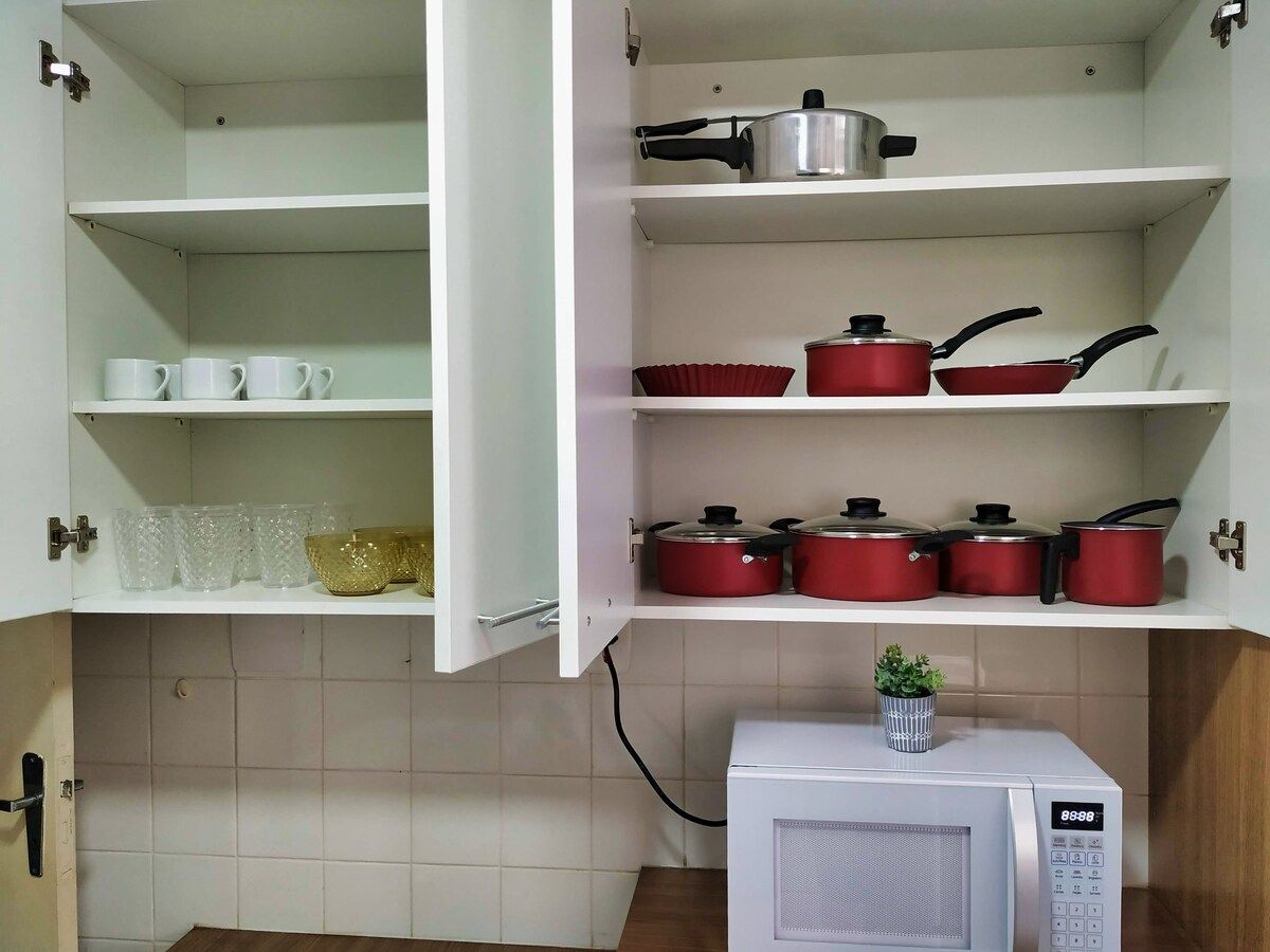 Una cocina con armarios blancos, un microondas y utensilios de cocina rojos en los estantes.