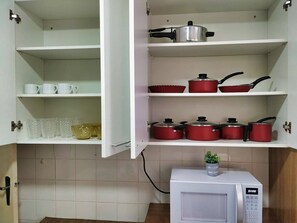 A kitchen with white cabinets, a microwave, and red cookware on the shelves.