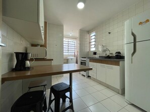 A kitchen with white cabinets, a wooden countertop, a coffee maker, a refrigerator, and a window with blinds.