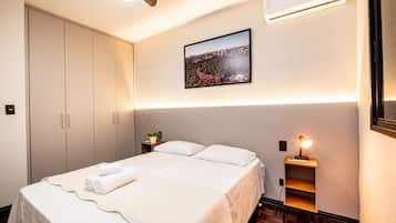 A hotel room with a bed, a nightstand, a wall-mounted air conditioner, and a framed picture on the wall.