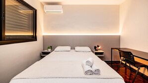 Ein Hotelzimmer mit einem Bett, einem Schreibtisch, einem Sessel, einem Nachttisch und einer Wand-Klimaanlage.