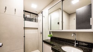 Ein modernes Badezimmer mit einer Duschkabine aus Glas, einem Waschbecken mit schwarzer Granitplatte und einem Spiegel darüber.