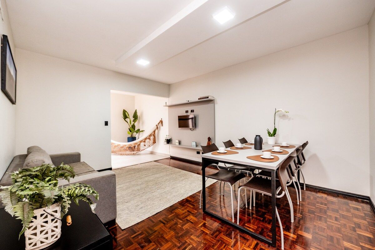 A modern living room with a sofa, a dining table with chairs, a coffee table, and a potted plant.
