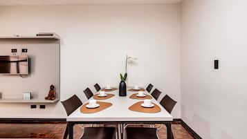 Sala de conferências com uma mesa branca, jogos americanos marrons e cadeiras pretas.