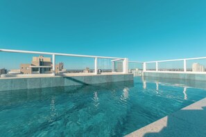 Une piscine sur le toit, avec une eau d’un bleu cristallin, entourée de bâtiments modernes et surplombant un ciel dégagé.