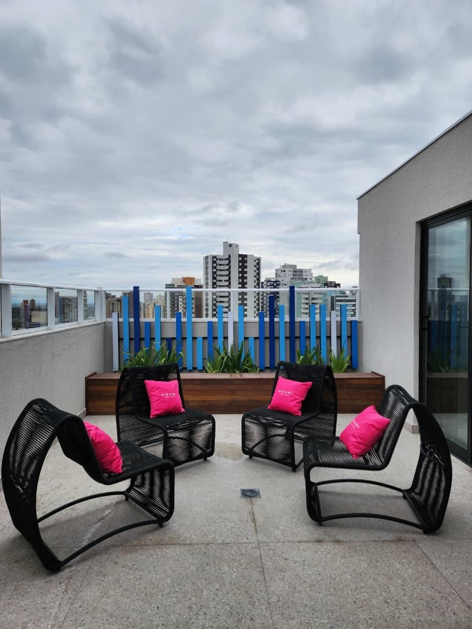 Una terrazza sul tetto con due poltrone in vimini nero, ciascuna con un cuscino rosa, e una vista sulla città sullo sfondo.