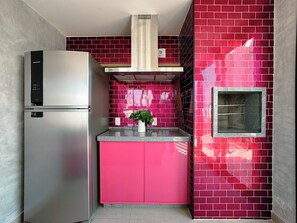 A compact kitchen with a stainless steel refrigerator, a pink cabinet, and a red-tiled backsplash.
