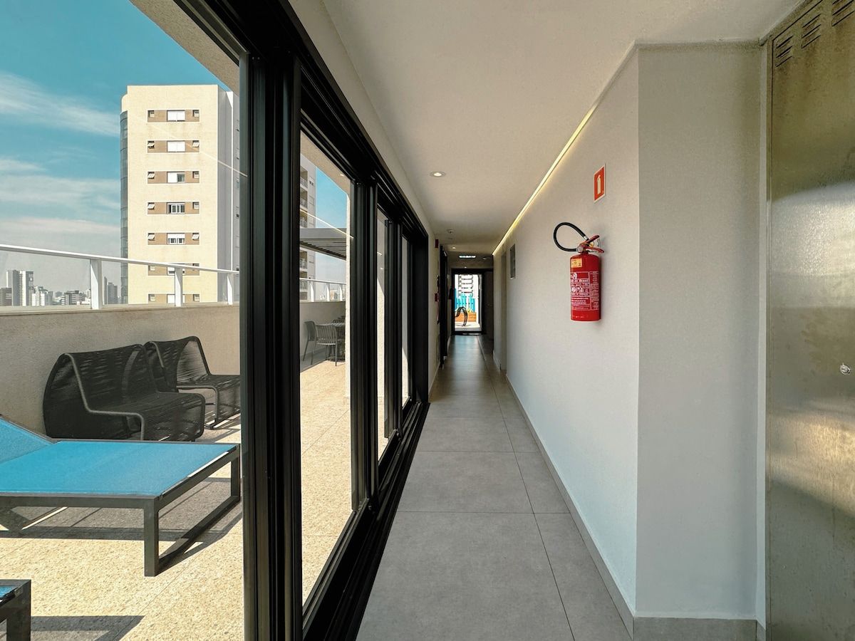 Ein Korridor mit einem an der Wand befestigten Feuerlöscher, einer Bank im Außenbereich und einem Blick auf ein Gebäude in der Ferne.