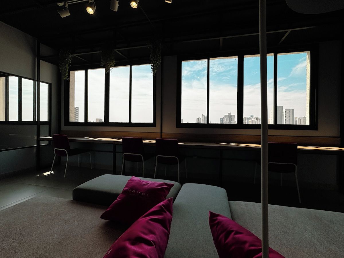 Una habitación de hotel moderna con un ventanal grande, un escritorio y un sofá con cojines.
