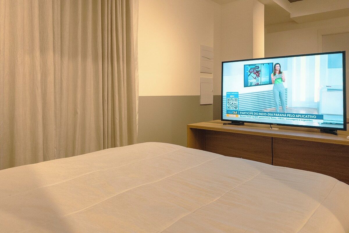 Una habitación de hotel con una cama, un televisor sobre un mueble de madera y una cortina.