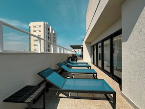 A rooftop terrace with sun loungers and a view of adjacent buildings.