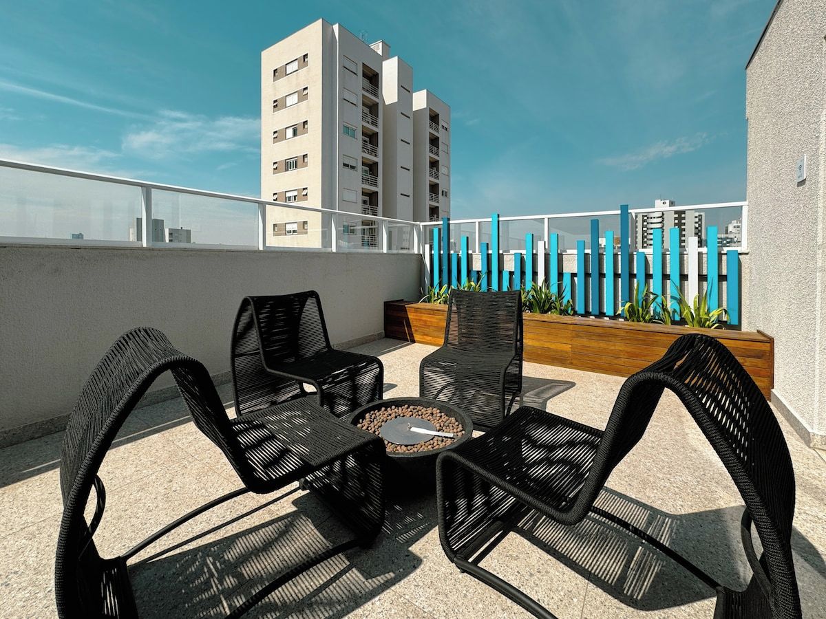 Eine Dachterrasse mit Korbmöbeln und einer Feuerstelle, mit Blick auf eine Stadtlandschaft.