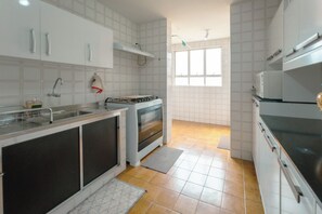 Een keuken met witte kastjes, een fornuis, een magnetron en een raam dat voor natuurlijk licht zorgt.
