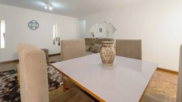 Un comedor con una mesa blanca, cuatro sillas, un jarrón decorativo y una alfombra estampada.