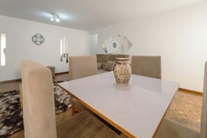 A dining area with a white table, four chairs, a decorative vase, and a patterned rug.