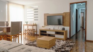Uma sala de estar moderna com sofá, TV, móvel para entretenimento em madeira e uma área de jantar com cadeiras e mesa.