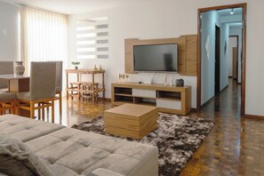 Een moderne woonkamer met een bank, televisie, een houten entertainmentkast en een eethoek met stoelen en een tafel.