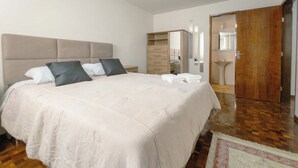 Quarto com cama grande, armário, espelho e banheiro visível por uma porta aberta.