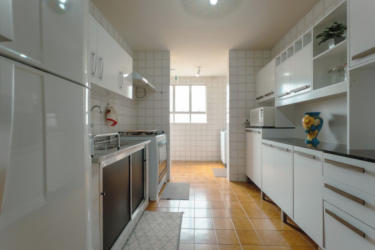 Cocina con gabinetes blancos, microondas y ventana que proporciona luz natural.