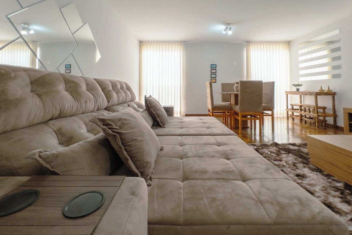 A modern living room with a large beige sofa, a dining area with a wooden table and chairs, and a fireplace.