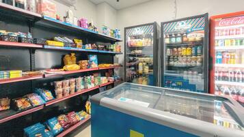 Interior de un supermercado con estantes llenos de diferentes productos alimenticios y dos dispensadores refrigerados de bebidas.