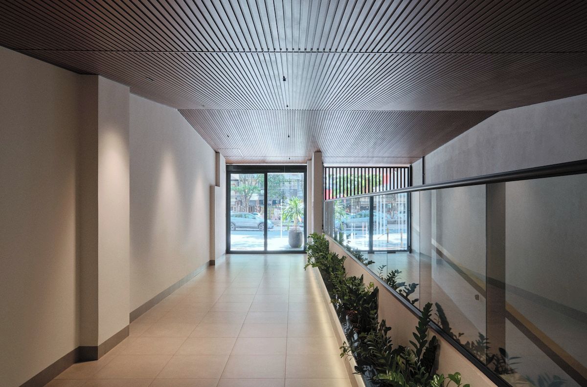 A corridor with a sloped ceiling, glass doors leading outside, and a plant-lined railing.