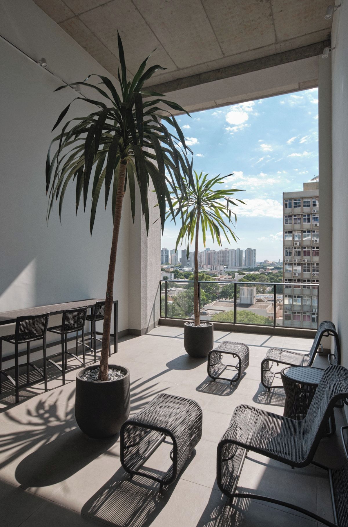 A balcony with a potted palm tree, outdoor seating, and a city view.