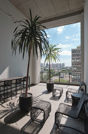 Un balcón con una palmera en maceta, mobiliario de exterior y vistas a la ciudad.