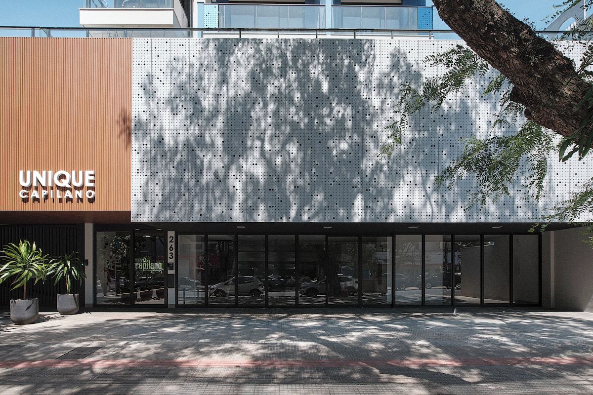 A modern building facade with a unique perforated panel design, a visible entrance, and a clear view of the street.