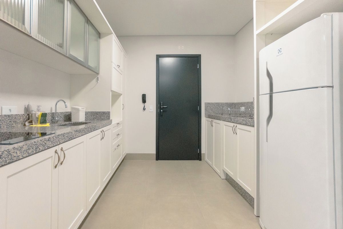 A narrow kitchen with white cabinets, a black door, and a white refrigerator.