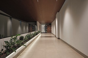Um corredor com teto de madeira, parede com plantas e chão de azulejos.