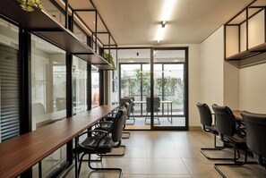 A modern office space with a long wooden table and black chairs, large windows, and a view of greenery outside. - Your Ideal Apartment in Downtown Maringa - CA1306 (Maringá)