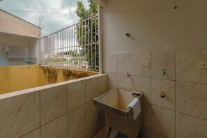 A bathroom with a bathtub, a sink, and a window with a metal fence. - Budget Apartment near Unicesumar - GI08 (Maringá)