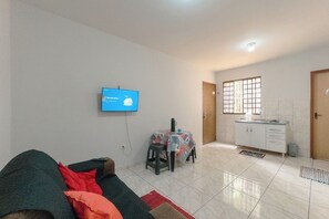 A living room with a sofa, a television mounted on the wall, a dining area with a table and chairs, and a kitchen area with cabinets and a window. - Budget Apartment near Unicesumar - GI08 (Maringá)