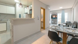 Cozinha moderna com bancada de mármore, iluminação pendente e área de refeições com mesa posta para quatro pessoas.