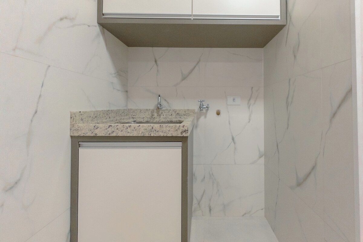A bathroom with a marble wall, a granite countertop, and a white cabinet.